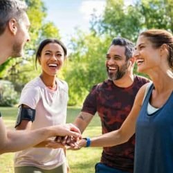 Laughing mature and multiethnic sports people putting hands together at park. Happy group of men and beautiful women smiling and stacking hands outdoor after fitness training. Multiethnic sweaty team cheering after intense training.